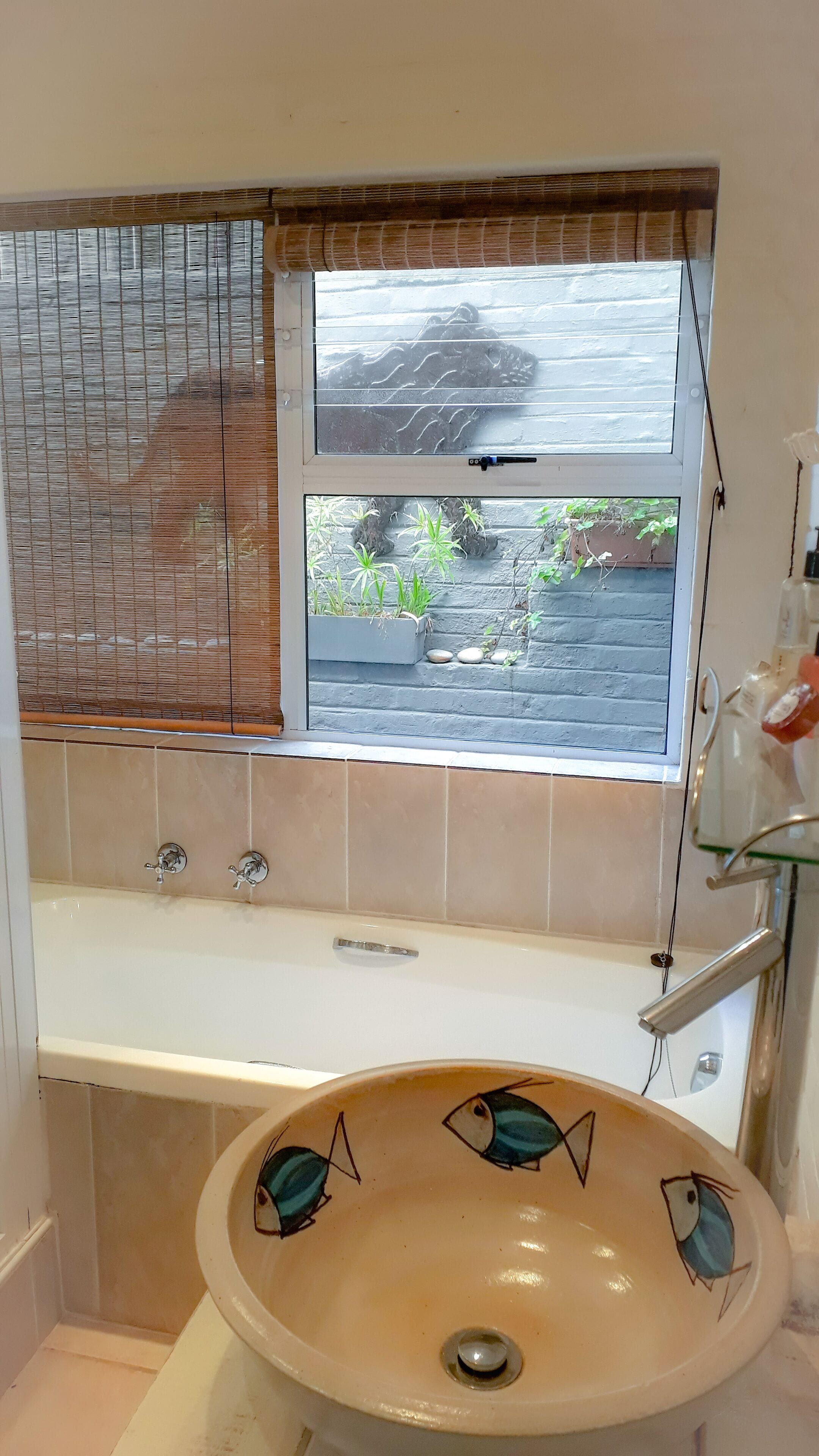 Une salle de bain avec une baignoire, un lavabo décoré de motifs de poissons, une fenêtre donnant sur des plantes et un espace douche.