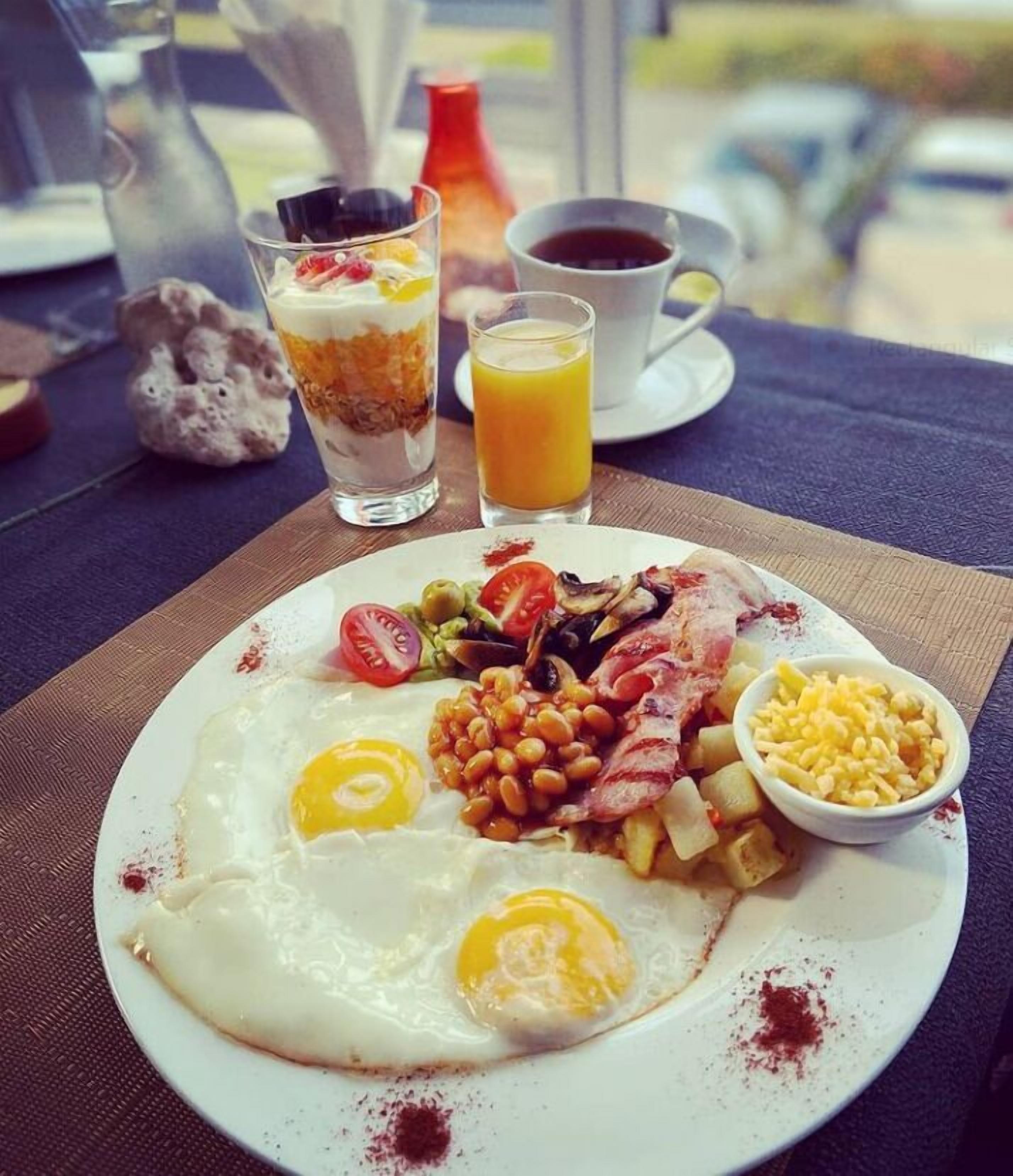 A breakfast plate with eggs, bacon, beans, corn, and tomatoes.