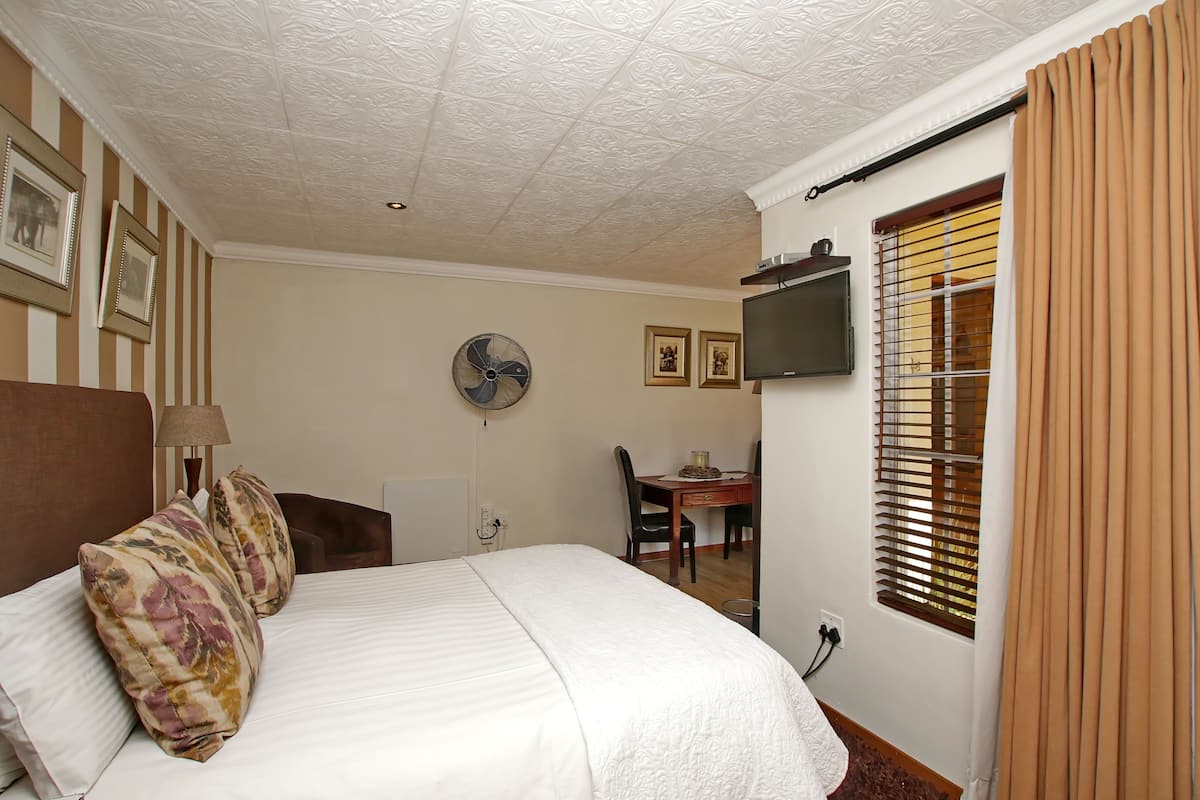 A hotel room with a bed, a desk, a chair, a television, and a window with blinds.