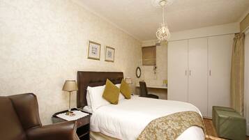 A hotel room with a bed, a chair, a desk, and a wardrobe.