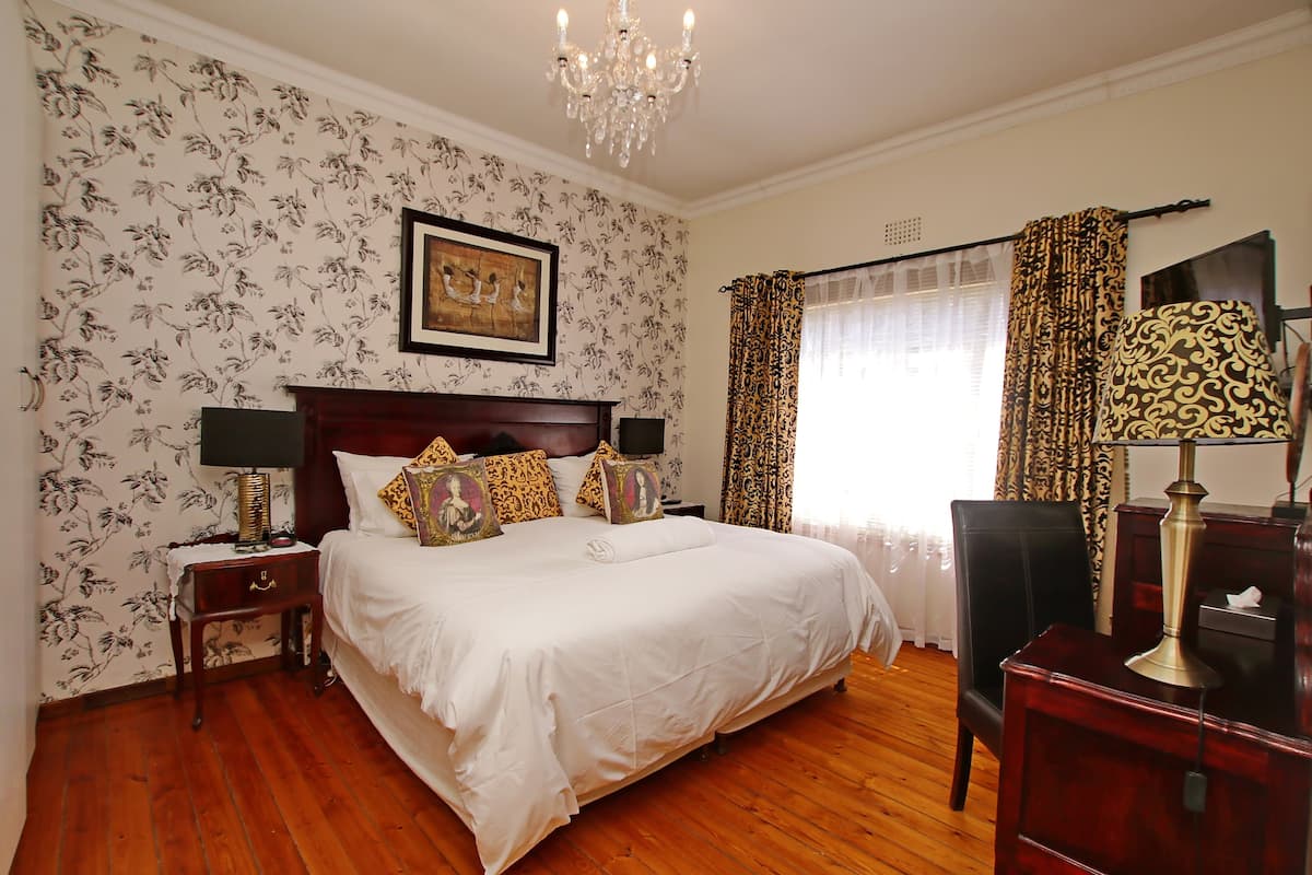 A neatly arranged bedroom with a large bed, two nightstands, a dresser, and a chandelier.