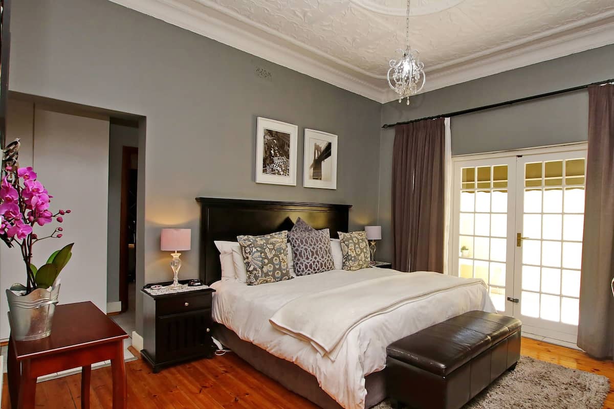 A bedroom with a large bed, a nightstand, a lamp, a vase with flowers, and a door with glass panels.