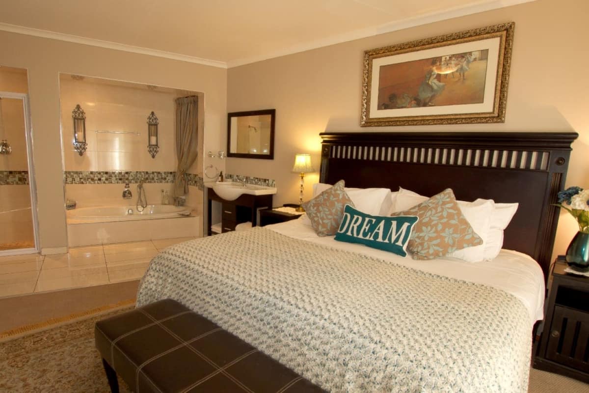 A hotel room with a large bed, a sitting area, a bathroom with a bathtub, and a painting on the wall.