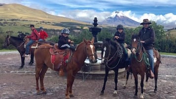 Eine Gruppe von Reitern in ländlicher Umgebung, im Hintergrund ein Brunnen und Berge.