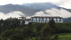 A large, multi-story building with a symmetrical facade, surrounded by lush greenery and mountains in the background. - CotopaxiPungo Finca Hotel (Rumipamba)