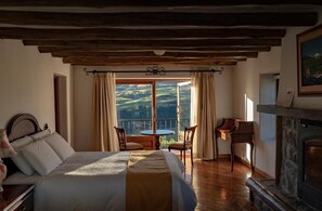 A bedroom with a large bed, a fireplace, a table with chairs, and a view of the outdoors. - CotopaxiPungo Finca Hotel (Rumipamba)