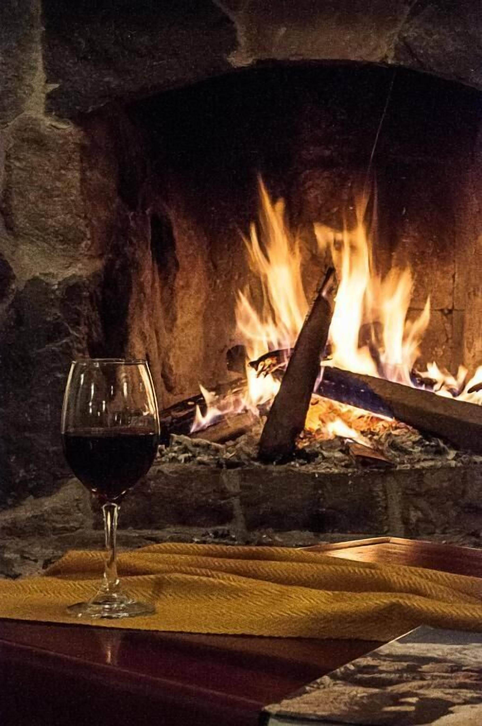 Um copo de vinho tinto sobre um guardanapo amarelo em frente a uma lareira com lenha acesa.