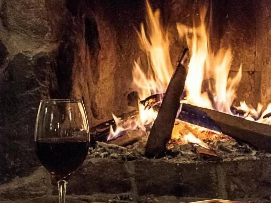 Um copo de vinho tinto sobre um guardanapo amarelo em frente a uma lareira com lenha acesa.