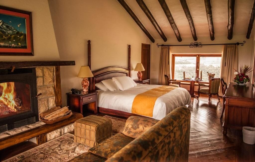 Een gezellige slaapkamer met een open haard, een groot bed, een bureau en uitzicht op de natuur.