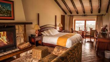 Een gezellige slaapkamer met een open haard, een groot bed, een bureau en uitzicht op de natuur.