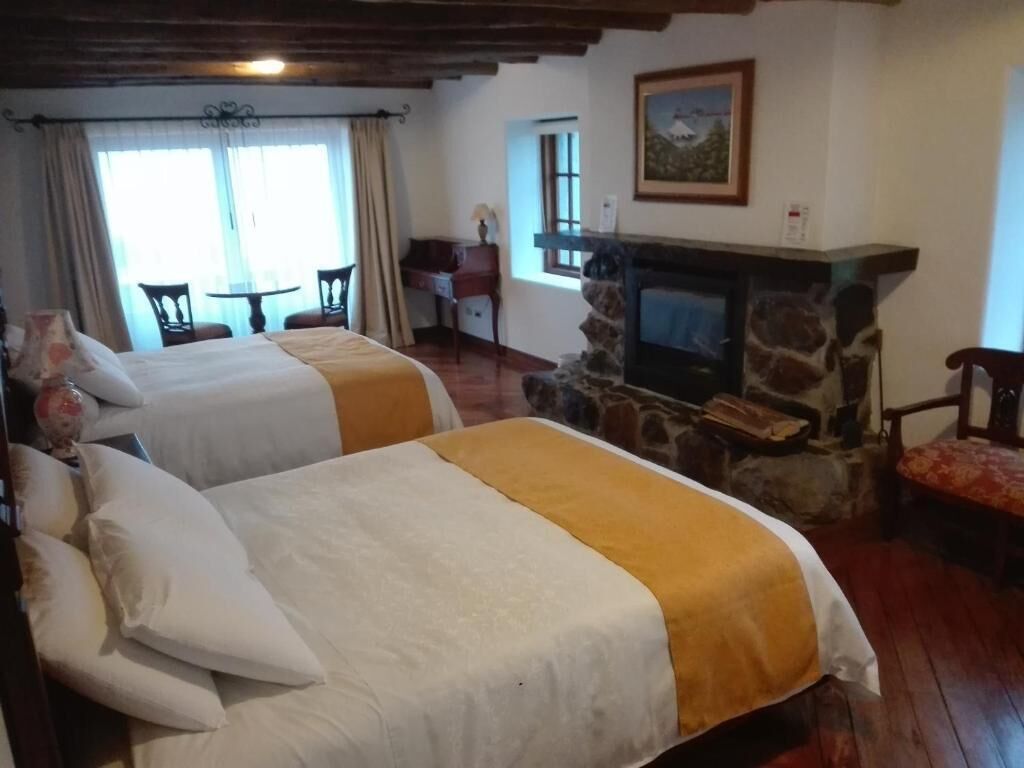 A room with two beds, a fireplace, a table, and a window.