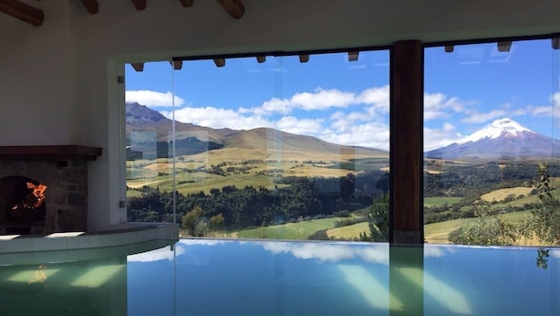Una habitación con piscina infinita de vidrio, chimenea de piedra y vistas a un paisaje montañoso.