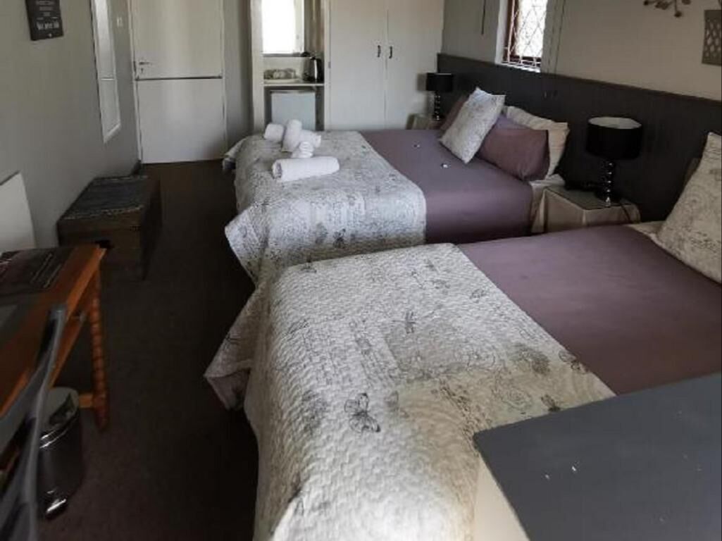 Une chambre d’hôtel avec deux lits, un bureau, une chaise, une armoire et une petite table avec une lampe.