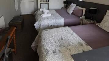 Une chambre d’hôtel avec deux lits, un bureau, une chaise, une armoire et une petite table avec une lampe.