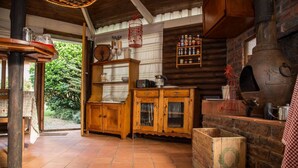 A rustic kitchen with wooden cabinets, a brick oven, and a shelf with various bottles. - Sunbird Guest House (Howick)