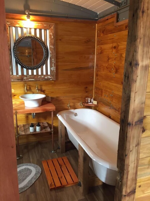 Un baño de cabaña de madera con una bañera independiente, un lavabo y un espejo.