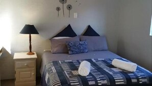 A bedroom with a bed, pillows, a nightstand, a lamp, and an air conditioning unit. - Sunbird Guest House (Howick)
