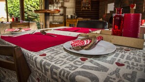 A dining table set with a red tablecloth, white plates, and a red vase. - Sunbird Guest House (Howick)