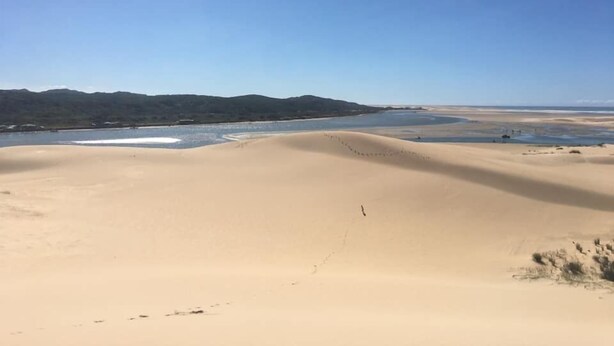 Un'ampia distesa sabbiosa sotto un cielo limpido, con dolci colline all'orizzonte.