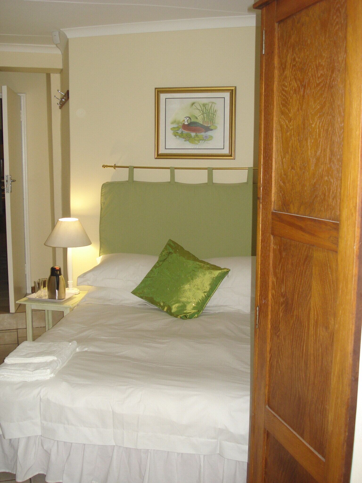 A hotel room with a bed, a nightstand with a lamp, a framed picture on the wall, and a wooden door.