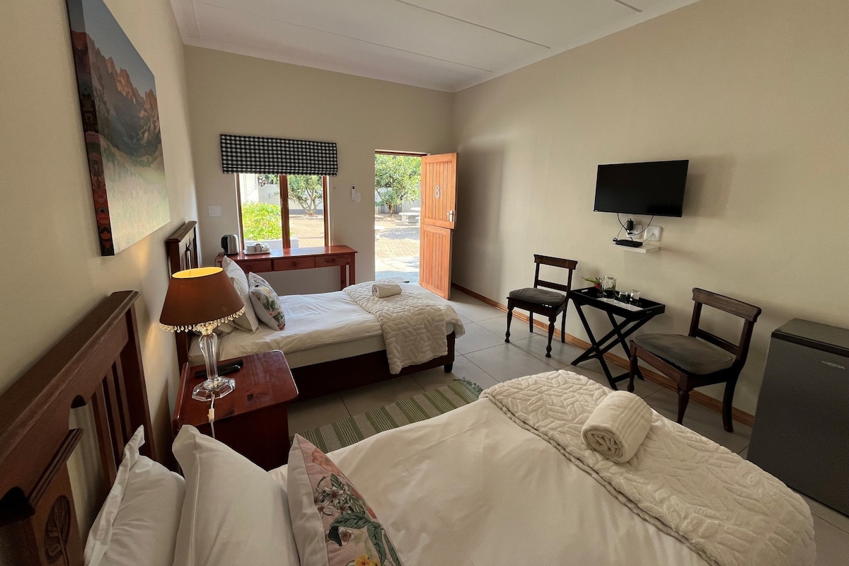 Ein Hotelzimmer mit zwei Betten, einem Schreibtisch, einem Sessel, einem Fernseher und einem Fenster mit Blick ins Freie.