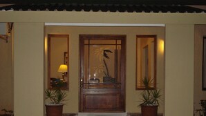 A wooden door with a glass panel and a palm tree design, flanked by two potted plants and a small step leading up to the door. - The Guest House Pongola (Pongola)