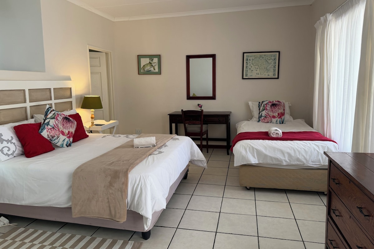 Ein Hotelzimmer mit zwei Betten, einem Schreibtisch, einem Stuhl und einem Deckenventilator.