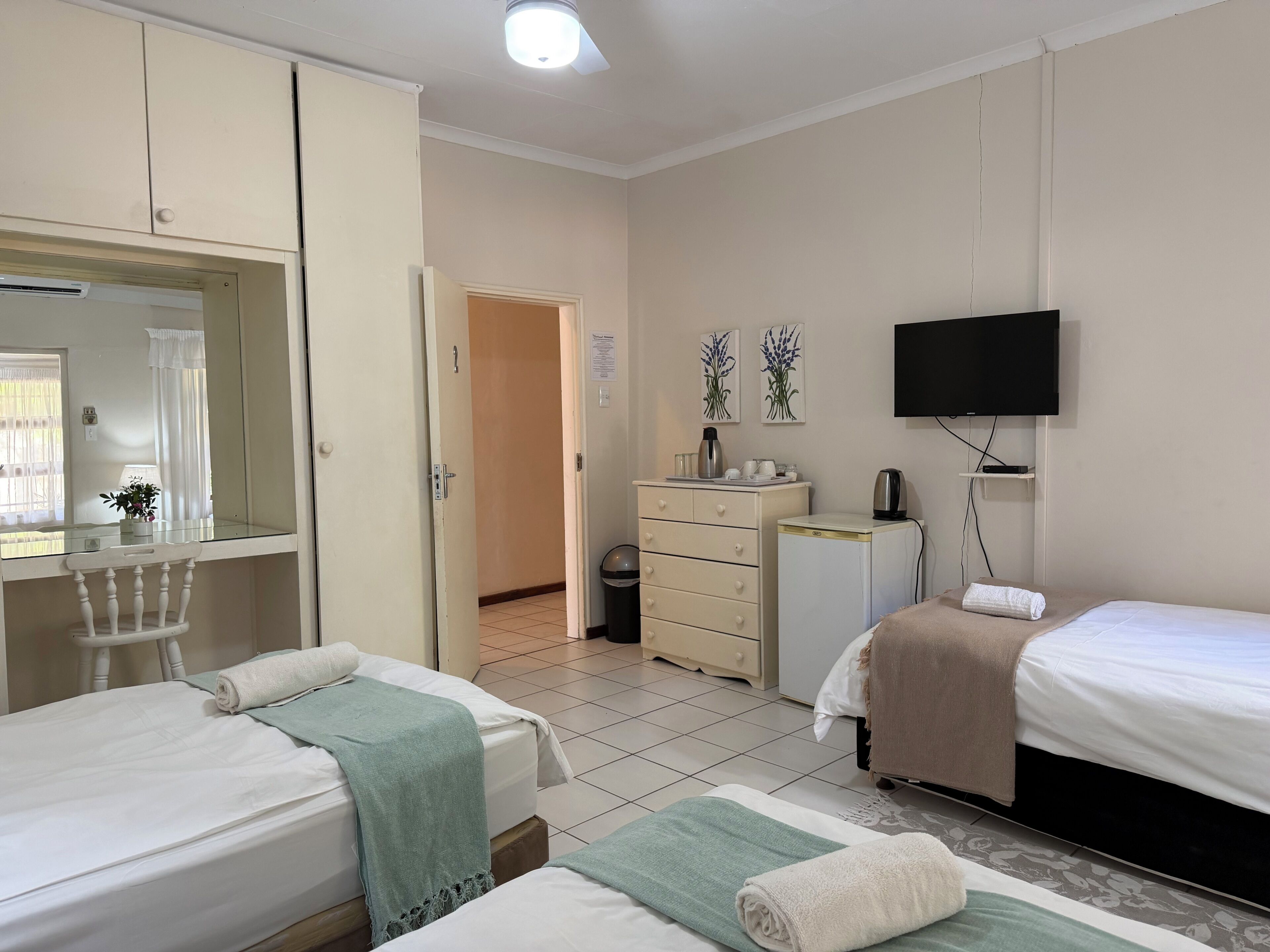 A hotel room with two beds, a television, a small refrigerator, a desk with a mirror, and a wardrobe.