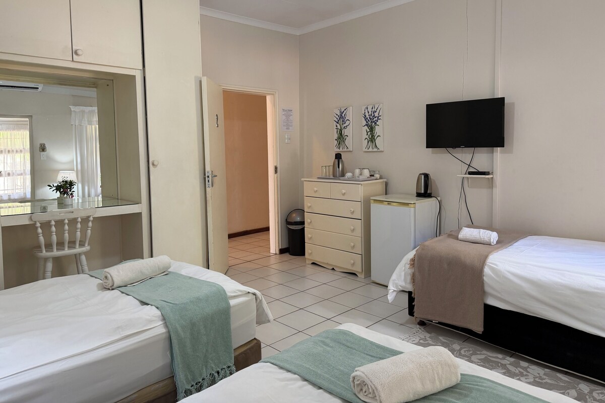 Ein Hotelzimmer mit zwei Betten, einem Fernseher, einer kleinen Kühlbox, einem Schreibtisch mit Spiegel und einem Kleiderschrank.