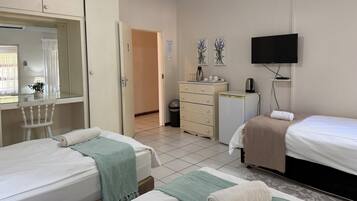 A hotel room with two beds, a television, a small refrigerator, a desk with a mirror, and a wardrobe.