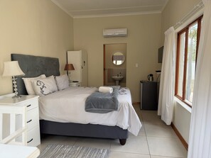 Ein Schlafzimmer mit Bett, Nachttischen, einer Lampe, einem Spiegel, einem Waschbecken und einem Fenster mit Vorhängen.