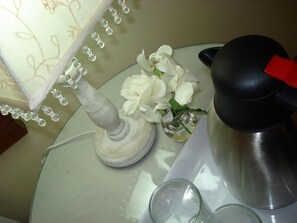 Une table avec une lampe, un vase contenant des fleurs blanches et un objet noir doté d’un manche rouge.