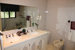 Une salle de bain avec deux lavabos, un miroir, un bidet et un meuble avec une poignée décorative.