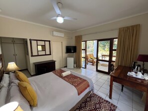 Ein Hotelzimmer mit einem Bett, einem Schreibtisch, einem Fernseher und einer Glastür zu einem Außenbereich.
