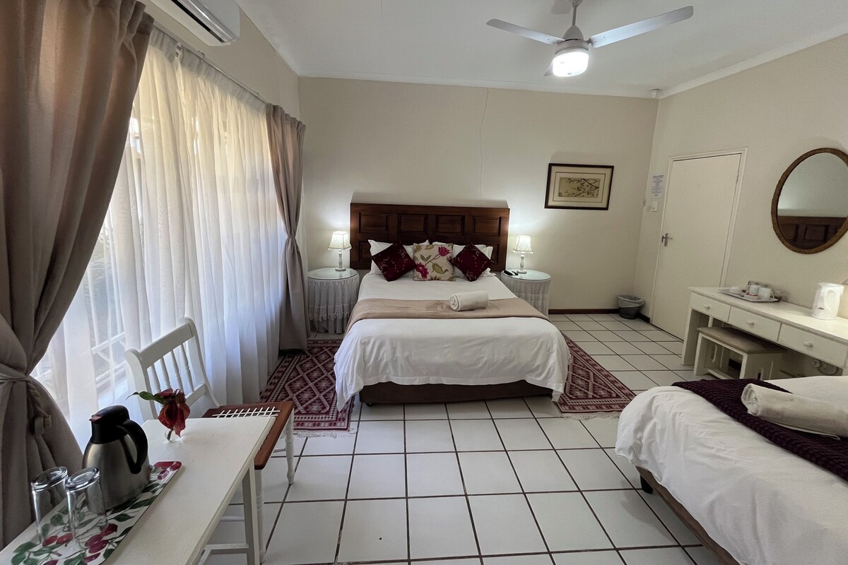 Ein Hotelzimmer mit Bett, Nachttischen, einem Schreibtisch mit Wasserkocher und einem Deckenventilator.