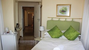 Een hotelkamer met een bed, nachtkastje met lamp, klein bureau met koffiezetapparaat en een lijst aan de muur.