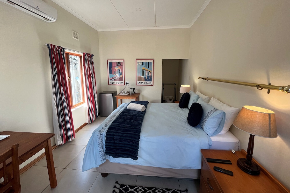 Ein Hotelzimmer mit einem Bett, einem Nachttisch, einer Lampe und einem kleinen Schreibtisch mit Stuhl.