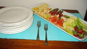 A table with a fruit platter, plates, and cutlery. - The Guest House Pongola (Pongola)