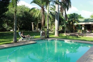 Piscina com espreguiçadeiras, cercada por palmeiras e uma área delimitada por cerca.