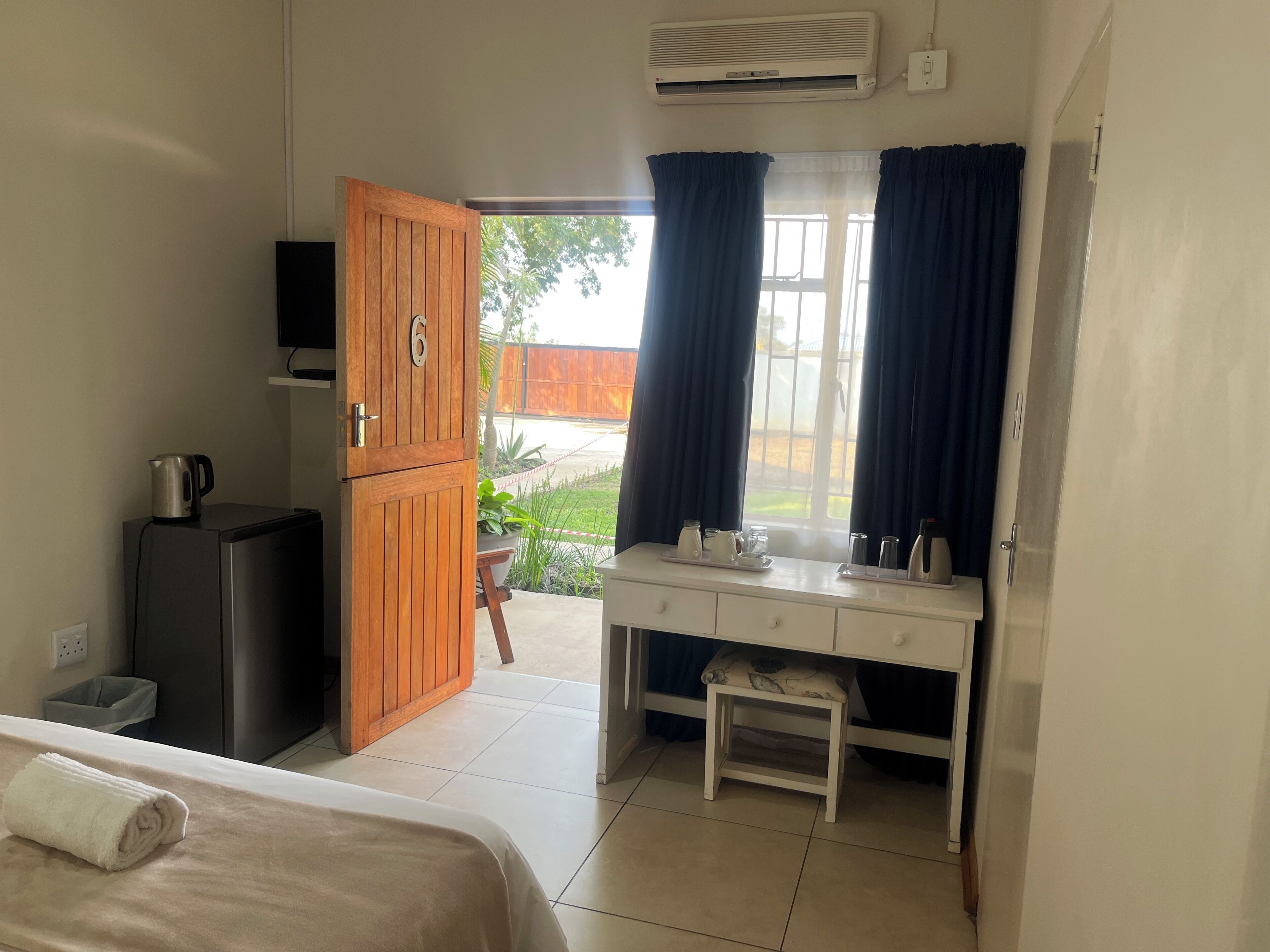 A room with a bed, a desk, a small table, a cabinet, and a window with curtains.