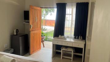 A room with a bed, a desk, a small table, a cabinet, and a window with curtains.