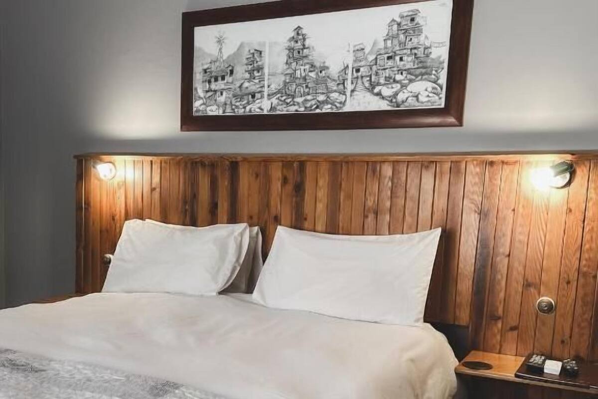 Une chambre à coucher avec une tête de lit en bois, un grand lit avec une literie blanche et une œuvre d’art encadrée au-dessus du lit.