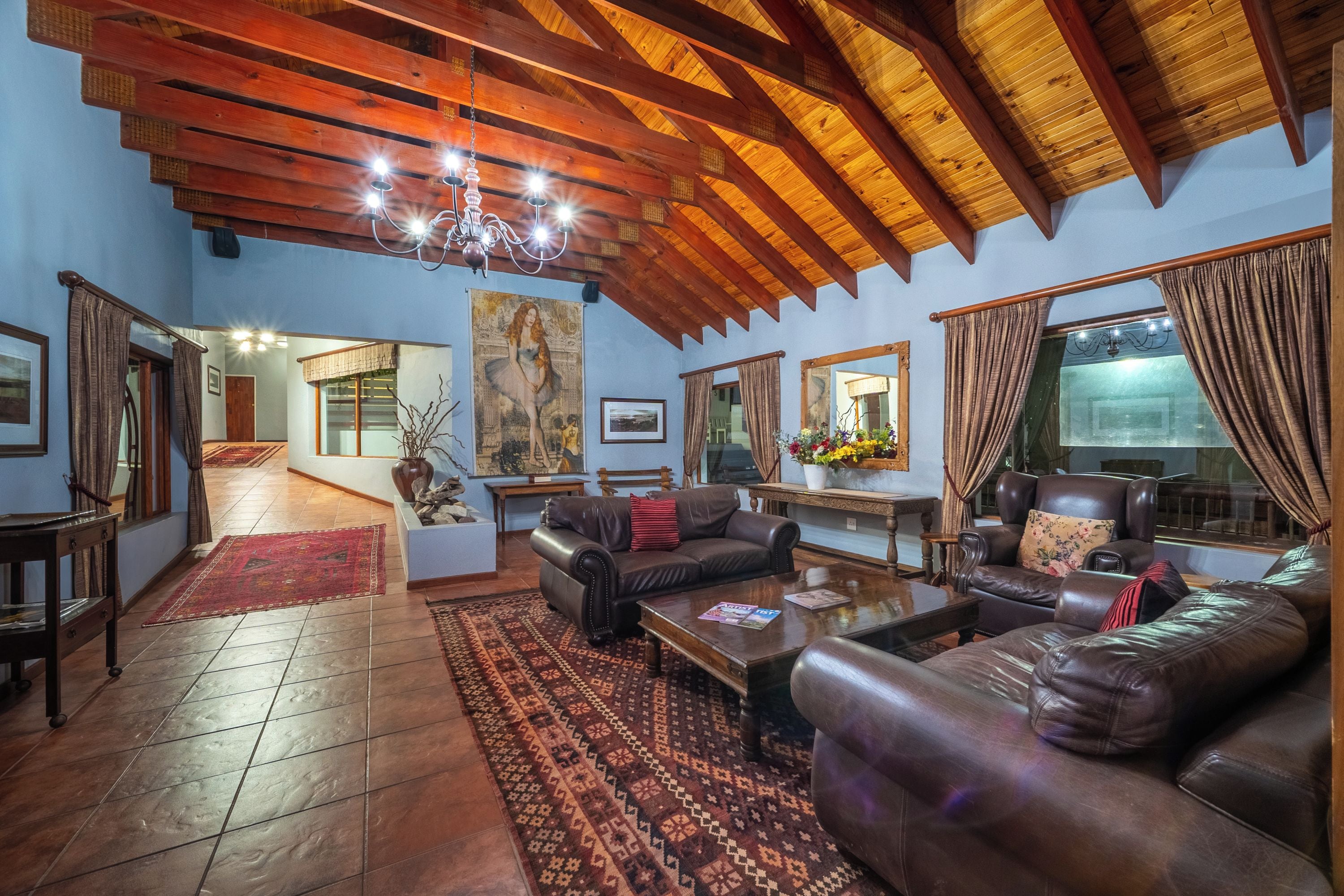 A spacious living room with a high wooden ceiling, leather sofas, a coffee table, and a large window with curtains.