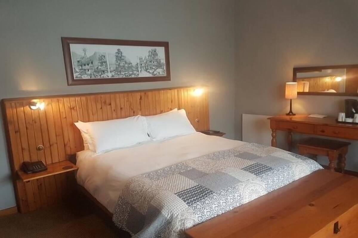 Un lit bien fait, avec une couverture à motifs, une tête de lit en bois, une lampe de chevet et une table de chevet sur laquelle se trouve un téléphone.