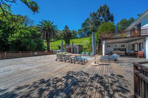 A wooden deck with lounge chairs and a pool area, surrounded by greenery and a building with a balcony. - Assegaaibosch Country Lodge (Kareedouw)