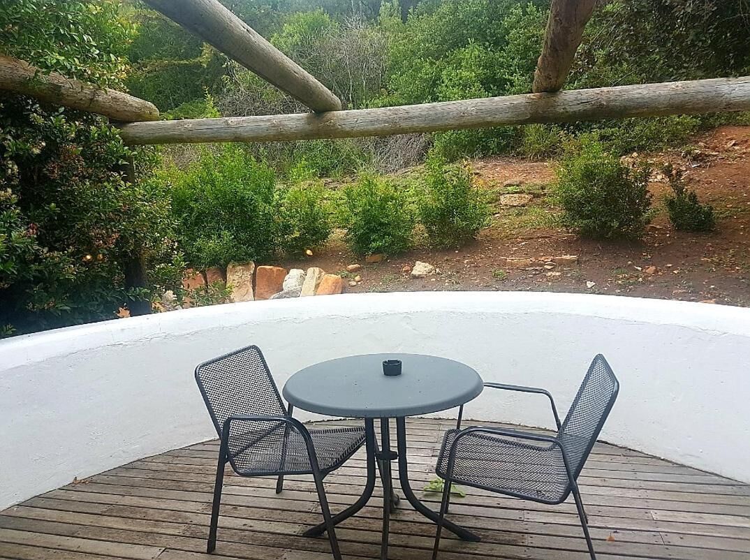 A covered outdoor seating area with a round table and two chairs, surrounded by a wooden deck and a white wall.