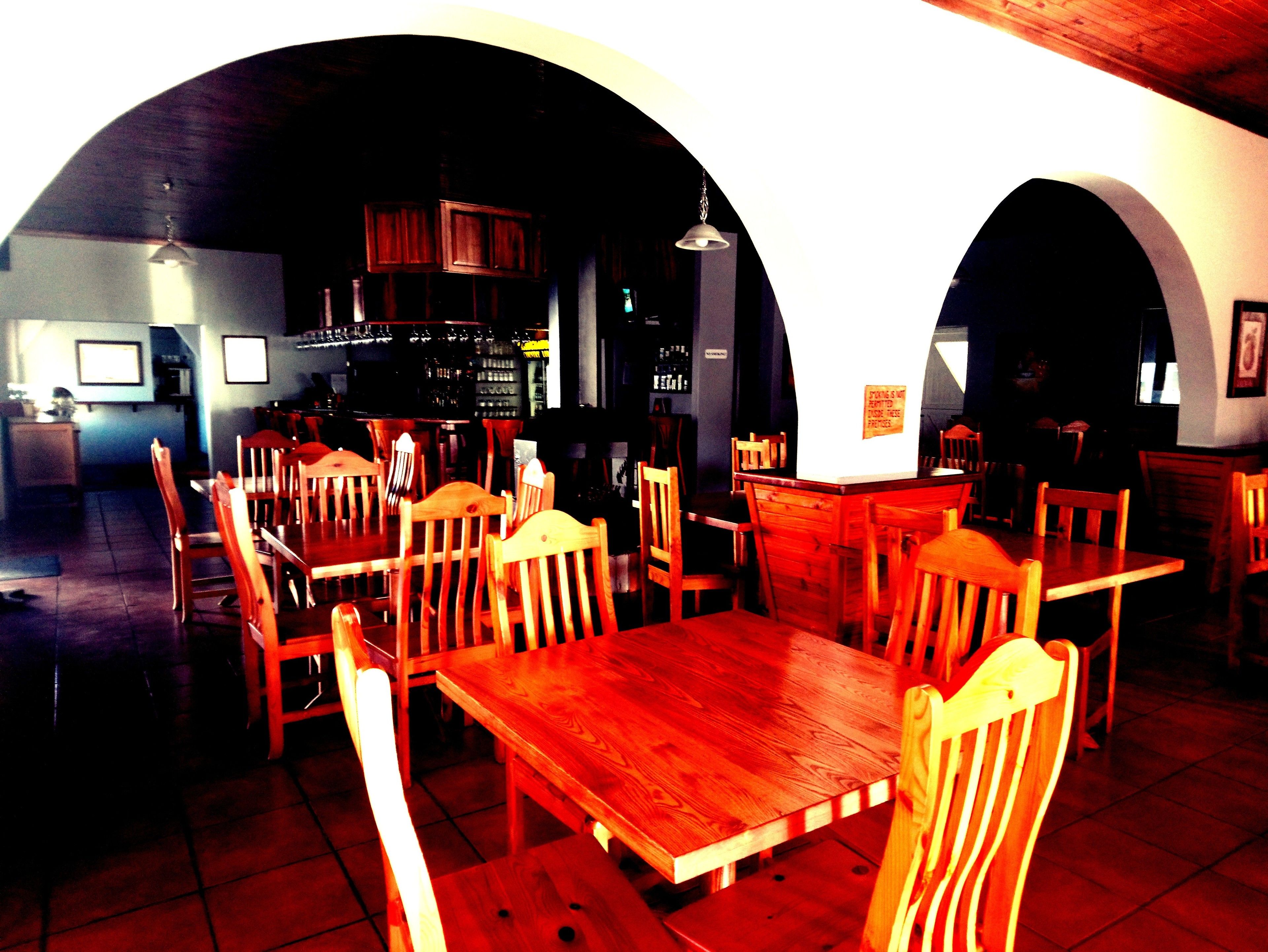 Un intérieur avec des tables et des chaises en bois, un coin bar avec des bouteilles et un panneau accroché au mur.