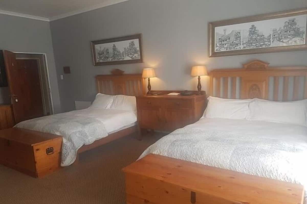 Une chambre d’hôtel avec deux lits simples, des têtes de lit en bois, des tables de chevet avec des lampes et un banc en bois.