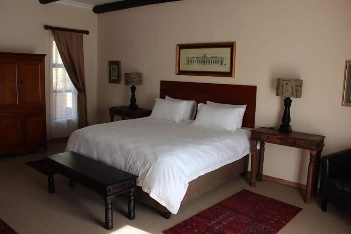 Une chambre avec un grand lit, un banc en bois, une table de chevet, un bureau et un tapis rouge.