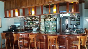 Een bar met houten toonbanken, meerdere barkrukken en een goed gevulde drankplank.